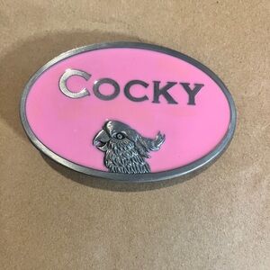 New pink Cocky" belt buckle is featuring the word "Cocky" in metallic letters